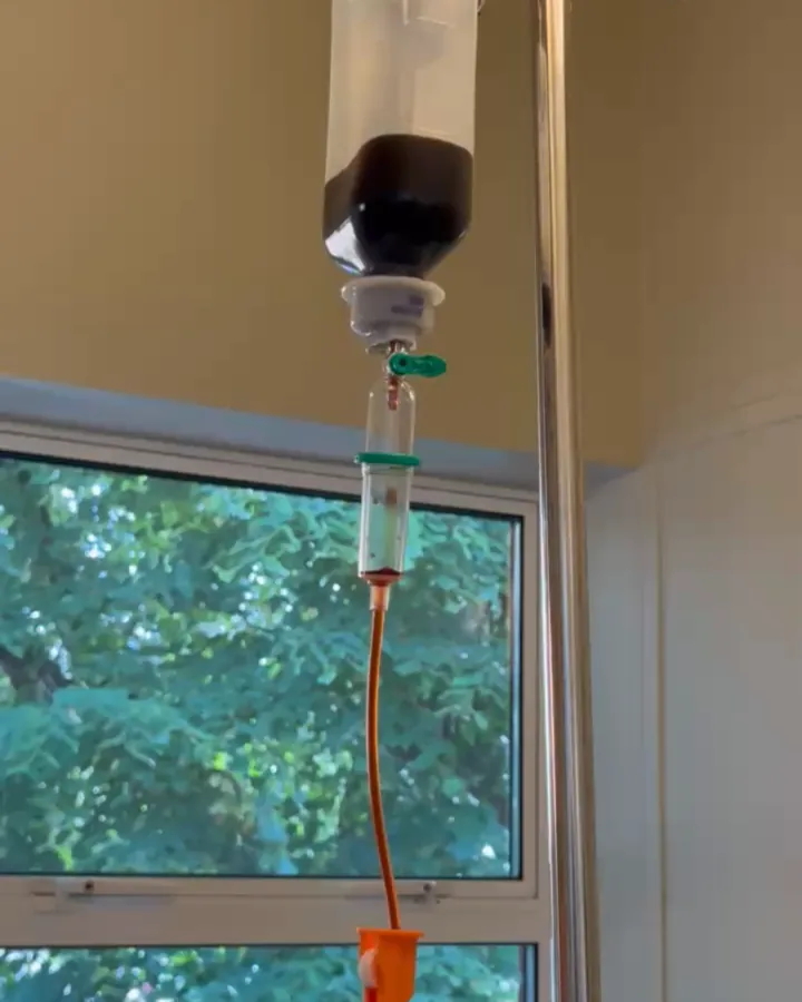 A bottle of intravenous iron hanging on a drip stand by a window at IronOx Clinic Cardiff, with the giving set and line attached